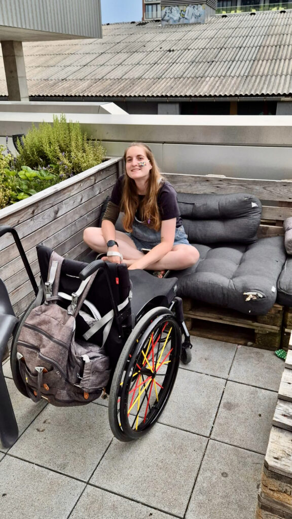 Mary is a white female and is seated on cosy cushions. Her wheelchair is in front of her