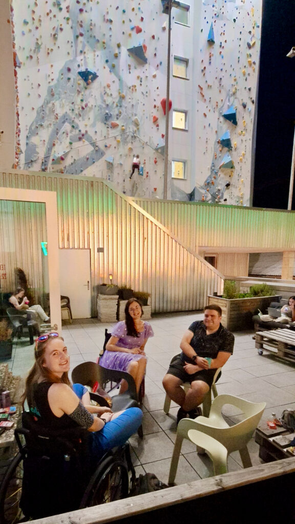 Group of people seated in an exterior balcony of the hostel. Climbing wall visible behind