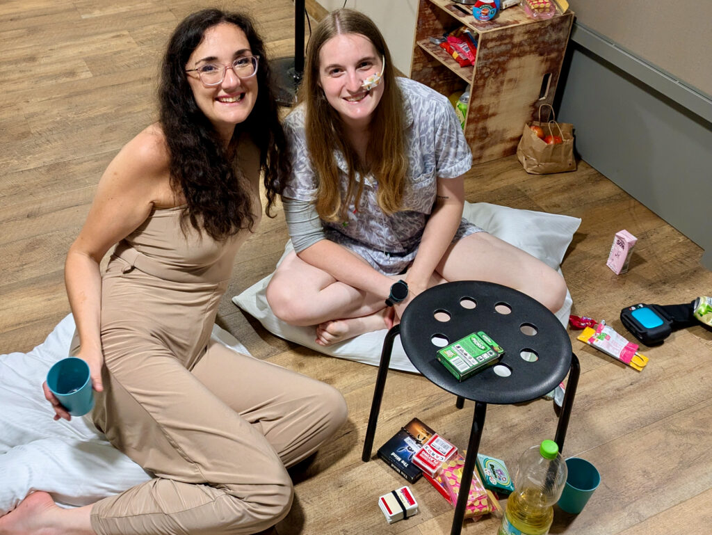 Mary and Georgina (white, brunette females) are seated on the floor in their hostel room in Werksviertel, Munich