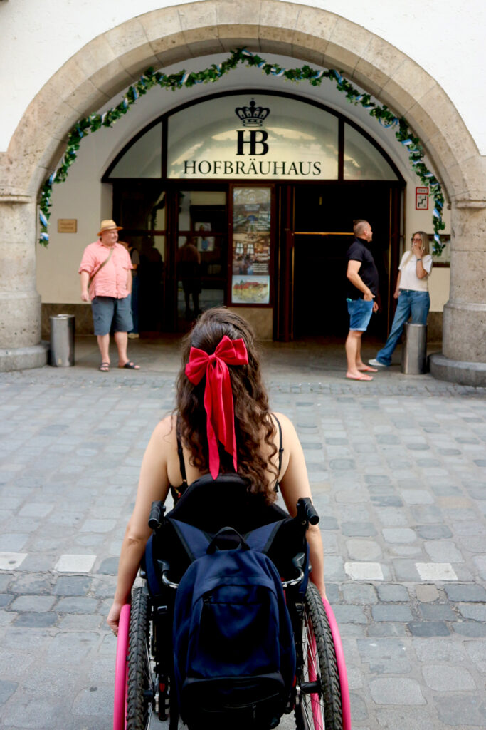 Georgina is seated in her wheelchair. You see the back of her head with a red bow