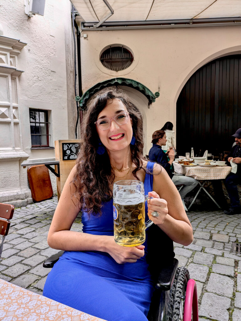 Georgina holding a large beer stein. She wears a blue dress and smiles at the camera