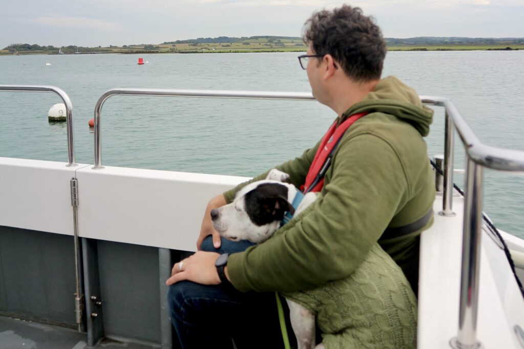 Richard sits on a bench with his dog, looking at the water