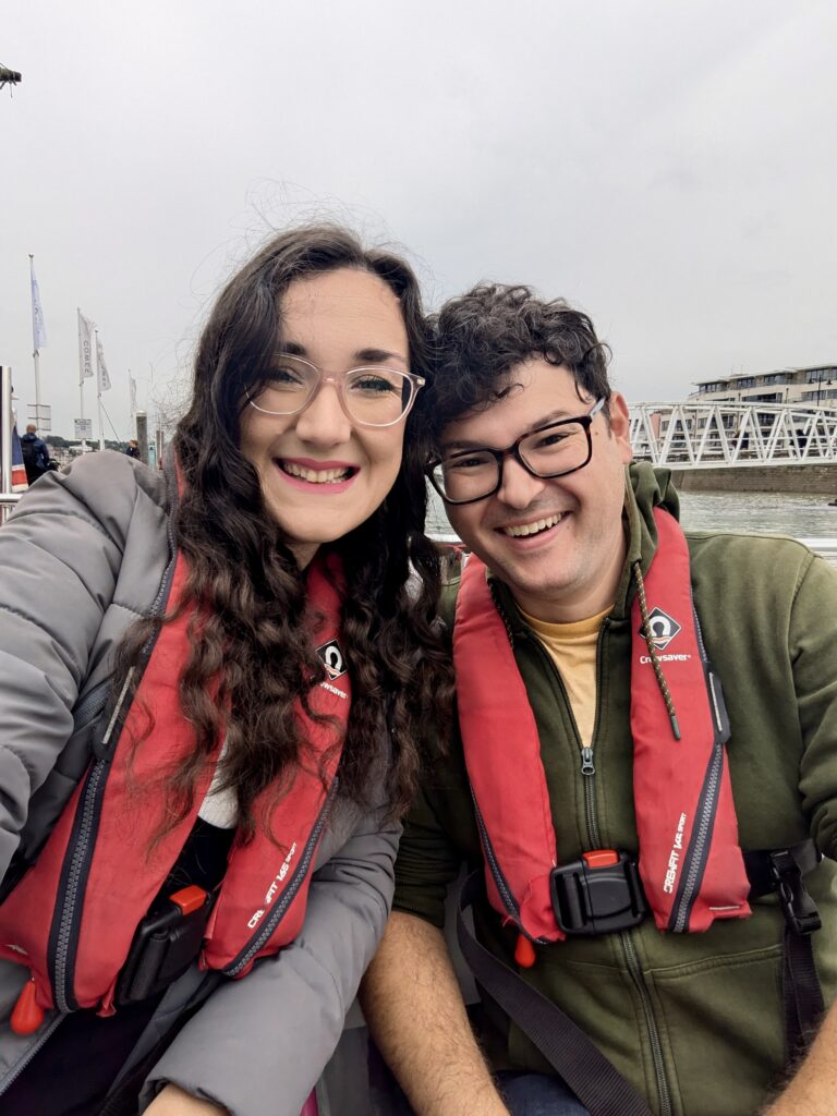 Selfie of Georgina and Richard, two white brunettes, with red life jackets onboard the accessible sailing experience with Wetwheels