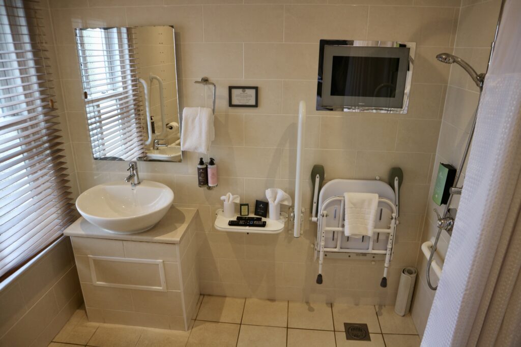 Accessible bathroom with collapsible shower seat and TV mounted in wall