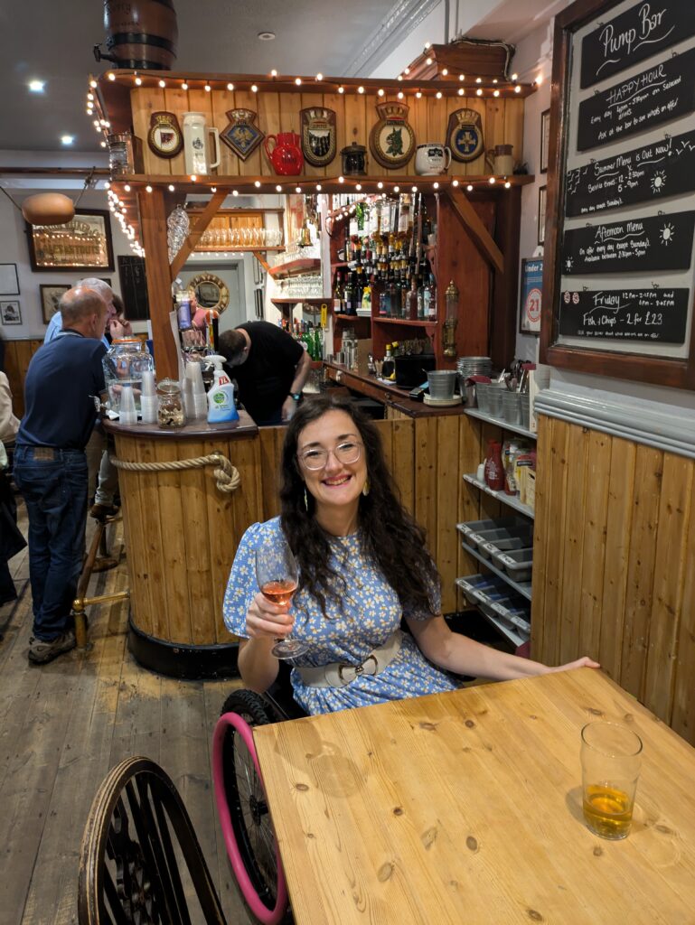 Georgina, a white brunette female who uses a wheelchair, smiles in The Pump Bar in The Seaview Hotel from her wheelchair.