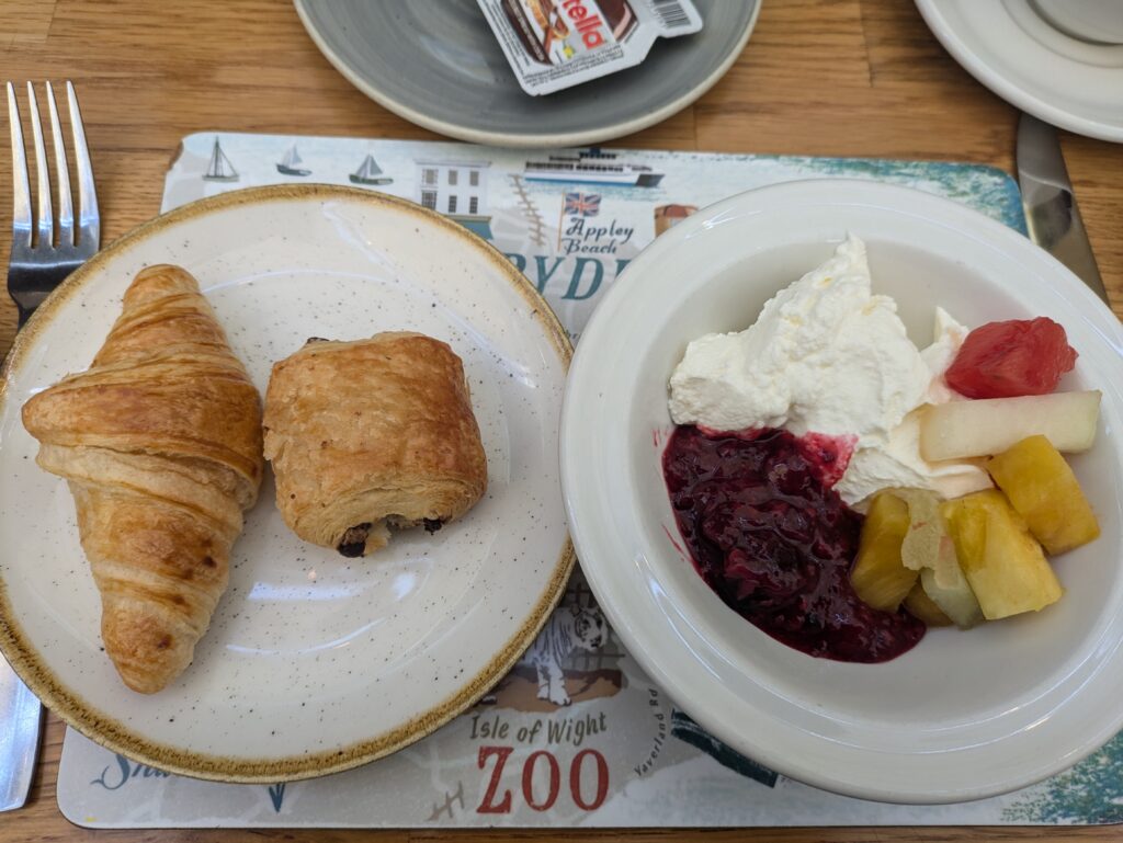 Two breakfast plates. One has a croissant & pain au chocolat and one has natural yoghurt with fruit salad.