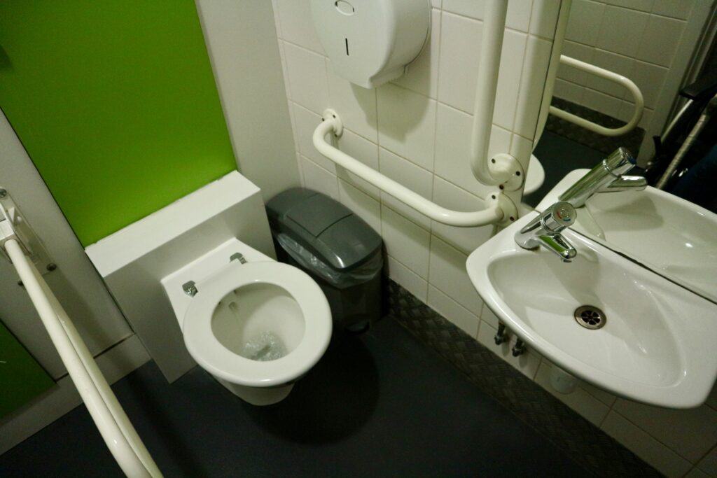 Interior of an accessible toilet. Two grab rails, a nearby sanitary bin and a lowered sink. Bright green walls.