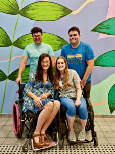 Four friends in front of a bright mural. Two are wheelchair users